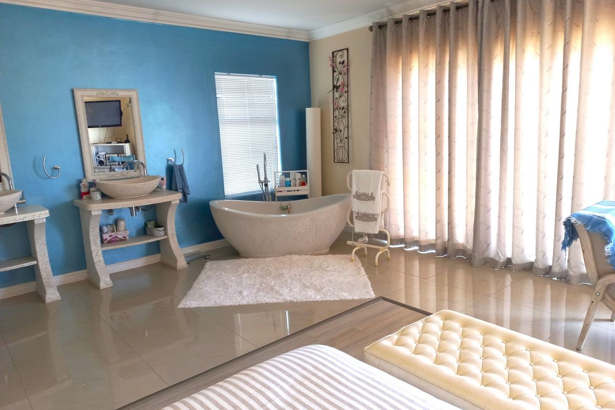 Spacious bathroom featuring a freestanding bathtub, dual vessel sinks on stone vanities, tiled flooring, and large windows with curtains.