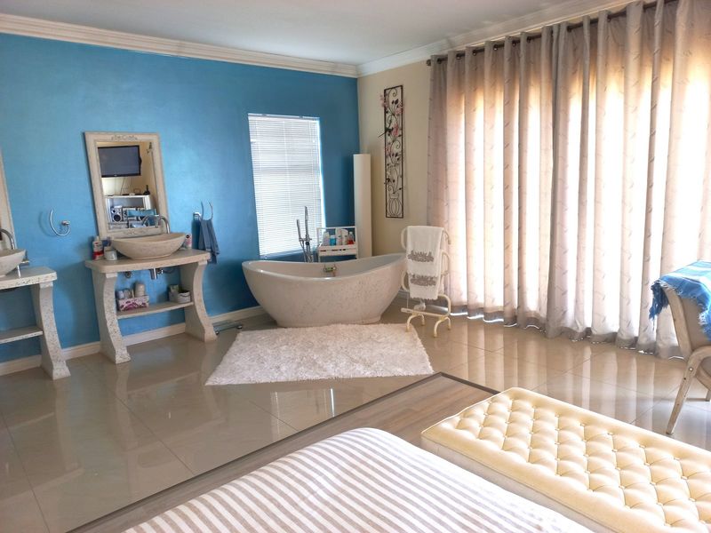 Spacious bathroom featuring a freestanding bathtub, dual vessel sinks on stone vanities, tiled flooring, and large windows with curtains.