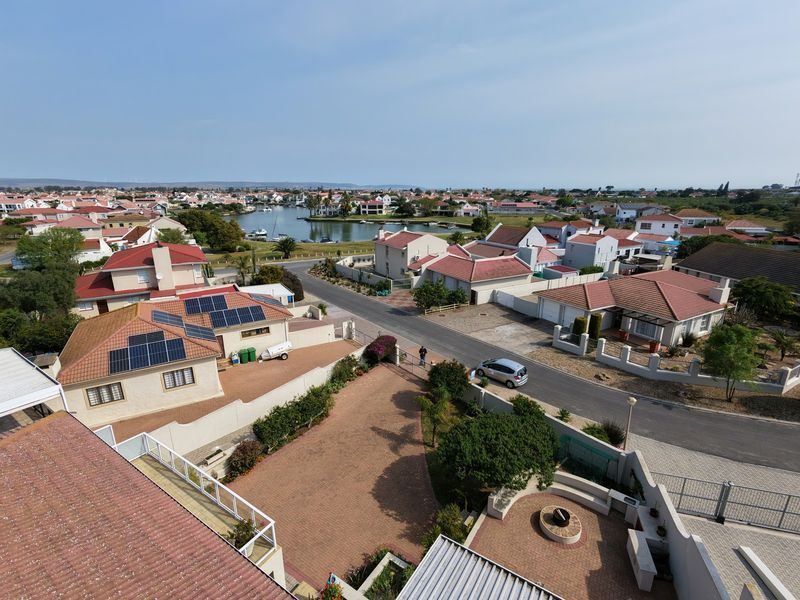 Aerial view of a residential estate featuring paved driveways, solar panels, and a communal fire pit area with surrounding neighborhood and lagoon views.