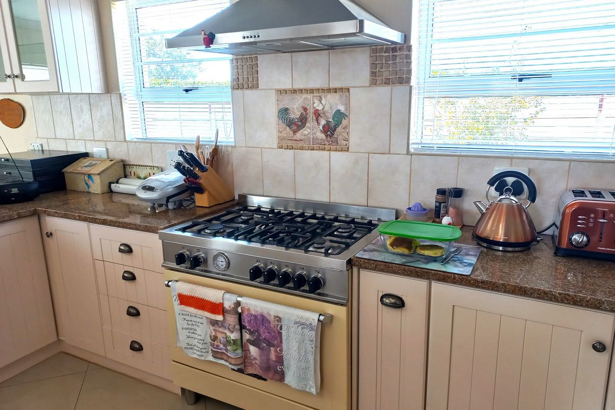 A functional kitchen featuring a gas stove, stainless steel extractor fan, granite countertops, and tiled backsplash with neutral cabinetry.