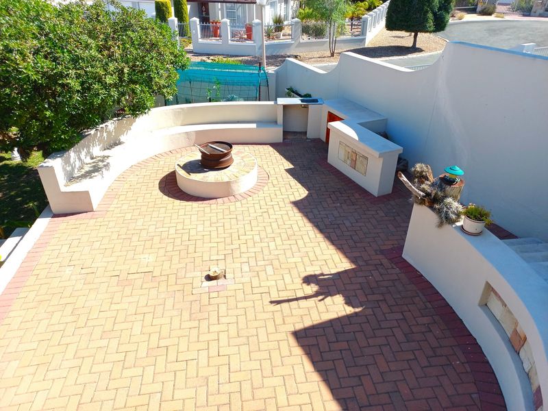 An outdoor patio area featuring built-in seating, a central fire pit, and a built-in braai station with a prep counter.
