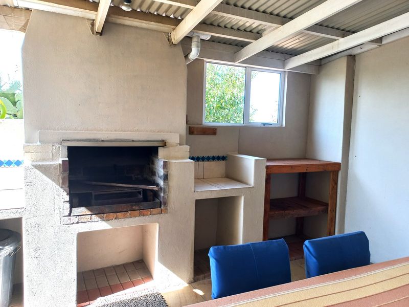 Covered outdoor patio area featuring a built-in brick braai, tiled prep counter, and exposed beam ceiling, ideal for outdoor entertaining.