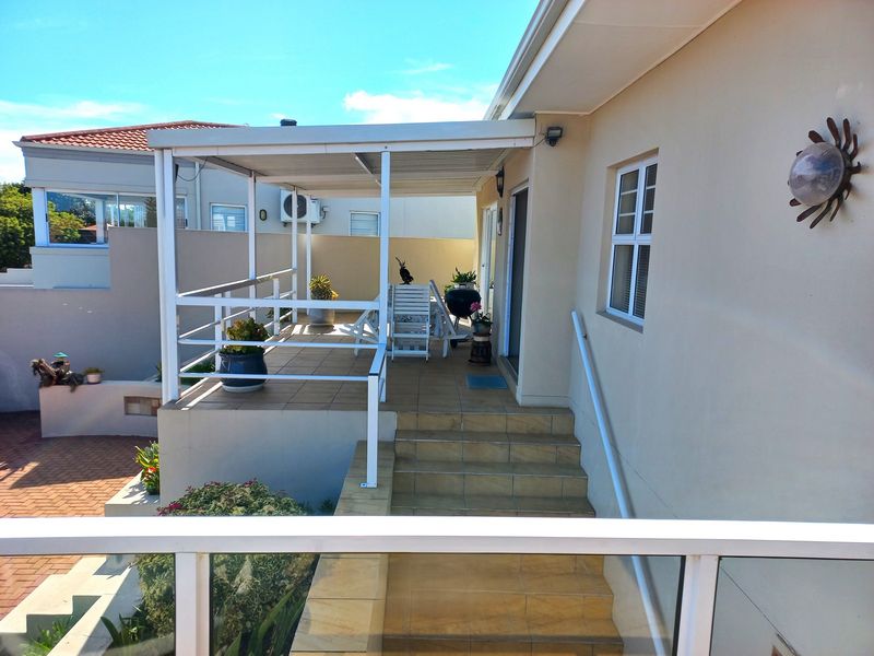 A covered outdoor patio area featuring tiled flooring, a metal balustrade, and steps leading down to the garden level.