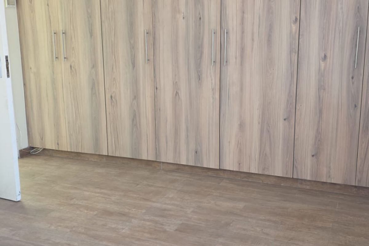 A clean, empty bedroom featuring modern wood-look laminate flooring and extensive floor-to-ceiling built-in cupboards with sleek handles.