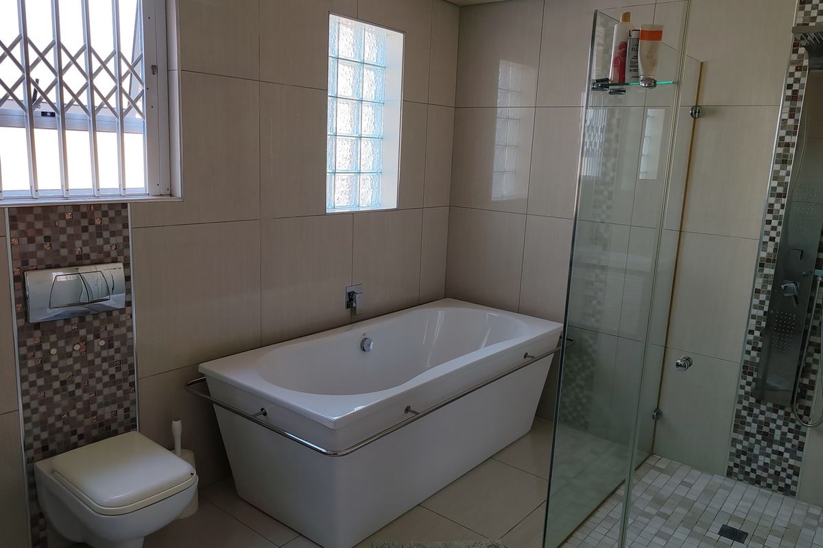 Modern bathroom featuring a wall-mounted toilet, a deep soaking bathtub, and a glass-enclosed walk-in shower with mosaic tile accents.