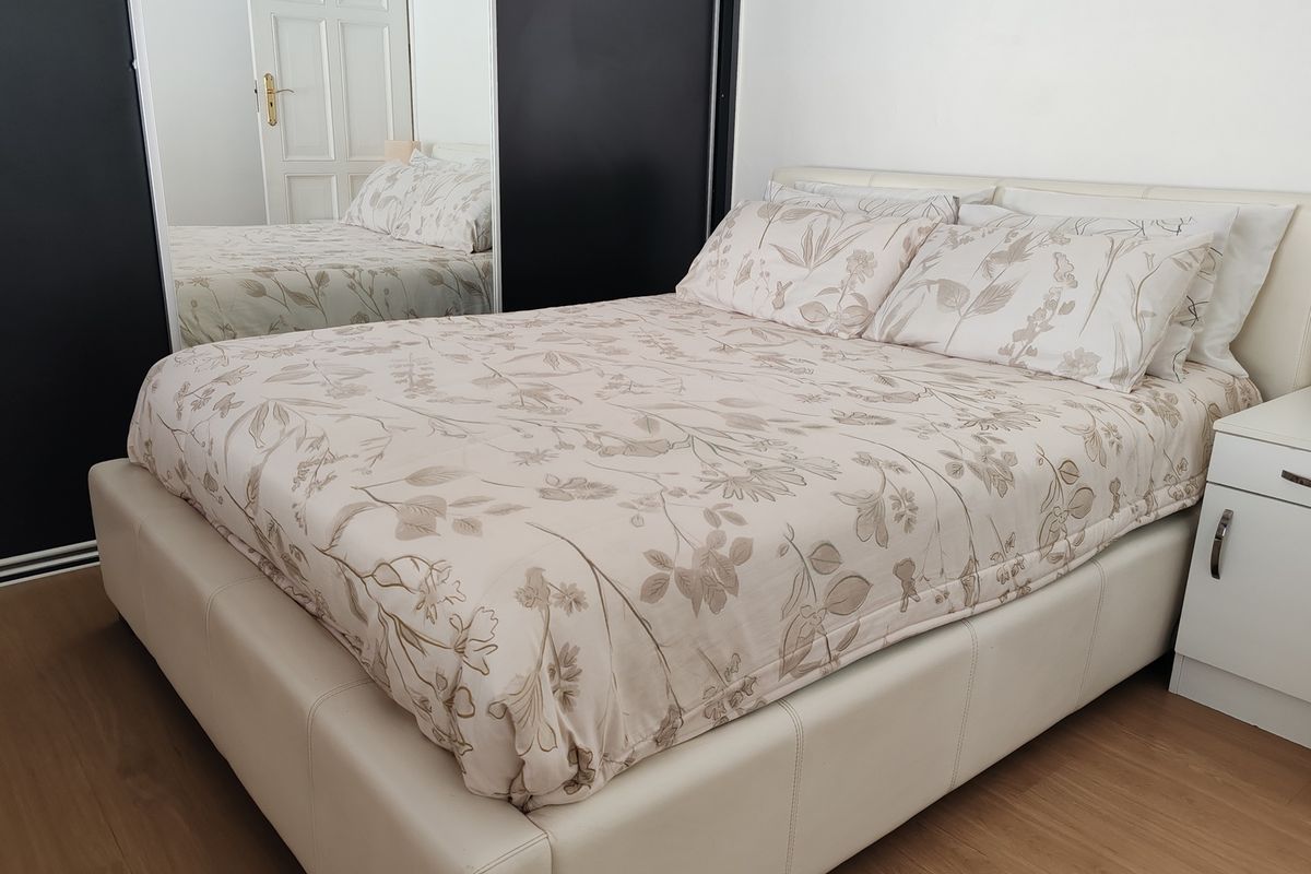 A well-maintained bedroom featuring built-in mirrored sliding wardrobes and light wood-look flooring.