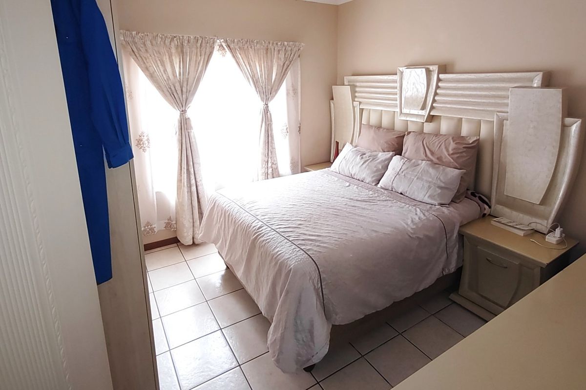A bedroom featuring tiled flooring and a window with curtains, providing a functional living space.
