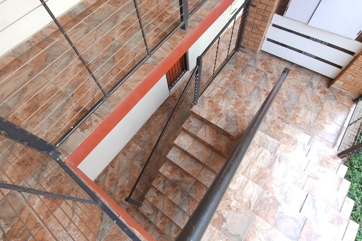An elevated view of an outdoor staircase featuring tiled steps, metal balustrades, and brickwork accents, providing access to the lower level of the property.