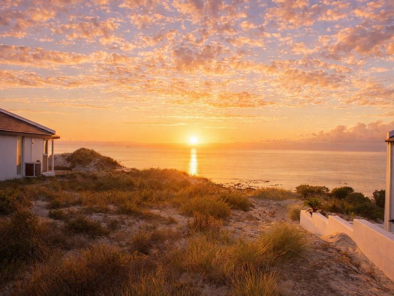 A stunning sunset view over the ocean, framed by coastal dunes and residential structures, highlighting the property's prime beachfront location.