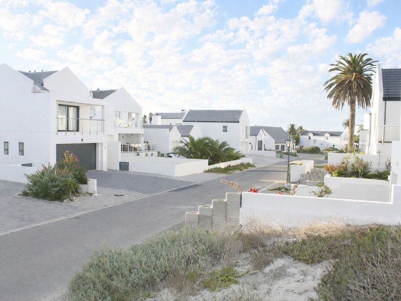 A street view of a residential estate featuring modern white houses with paved driveways and landscaped surroundings.
