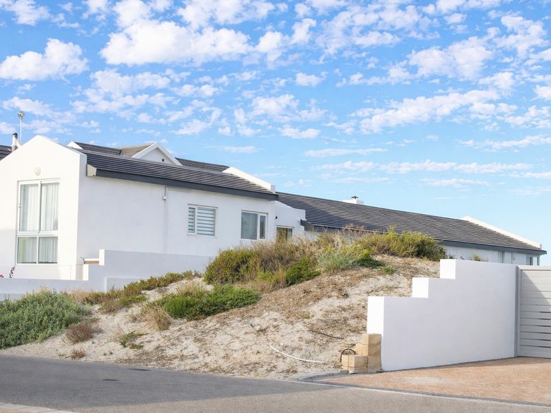 Front exterior view of a white residential property featuring a tiled roof, paved driveway, and a landscaped sand dune area with boundary wall.
