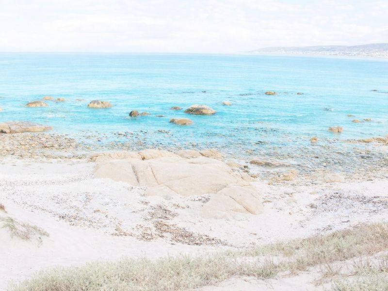A scenic coastal view featuring a sandy beach, rocky shoreline, and clear blue ocean waters.