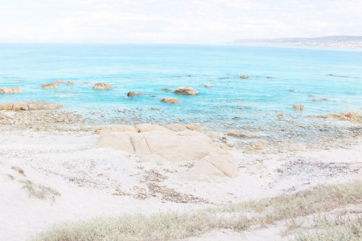 A scenic coastal view featuring a sandy beach, rocky shoreline, and clear blue ocean waters.