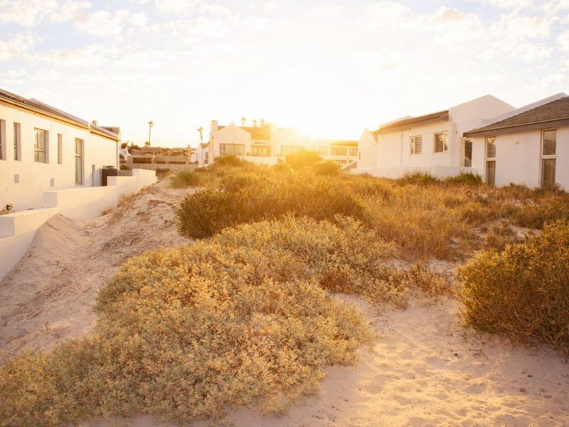 A view of the rear exterior area featuring natural sand dunes and coastal vegetation situated between residential buildings.