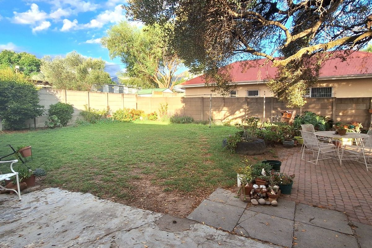 A spacious rear garden featuring a paved patio area, established lawn, and perimeter boundary walls, offering a private outdoor space.