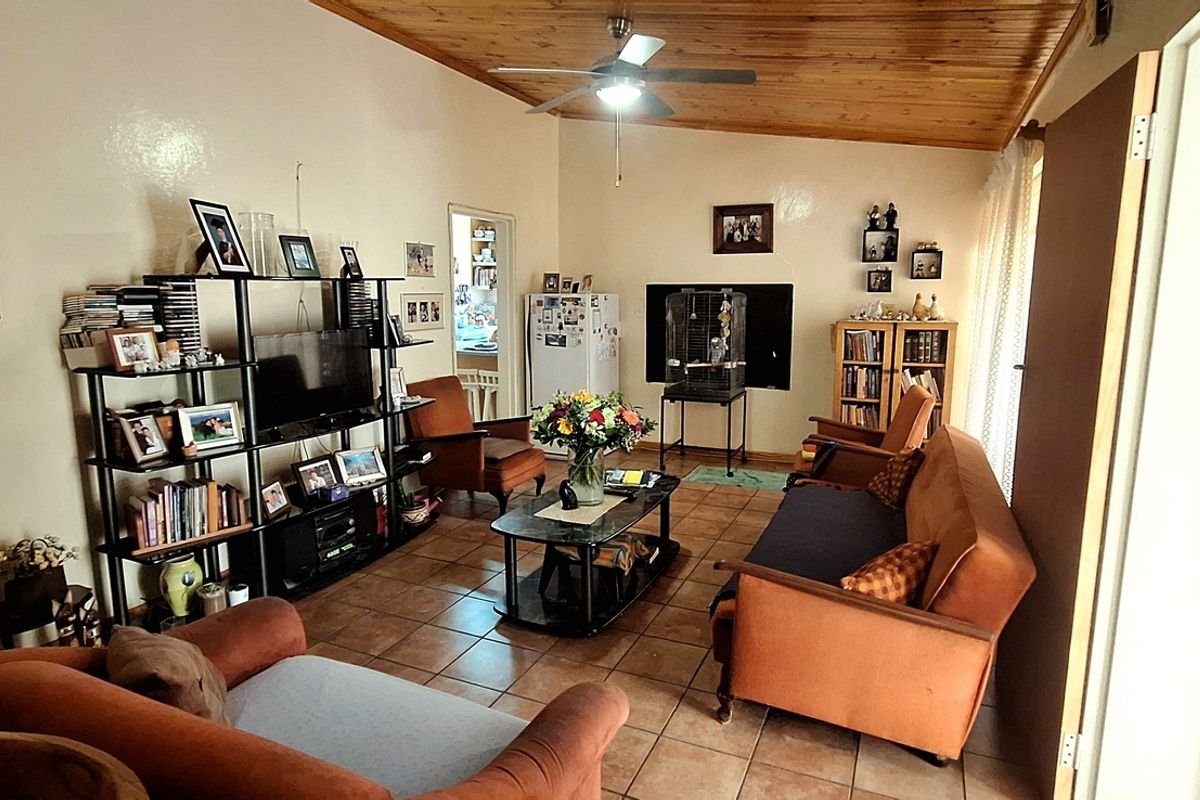 A comfortable living room featuring tiled flooring and a vaulted timber-clad ceiling with a central ceiling fan.
