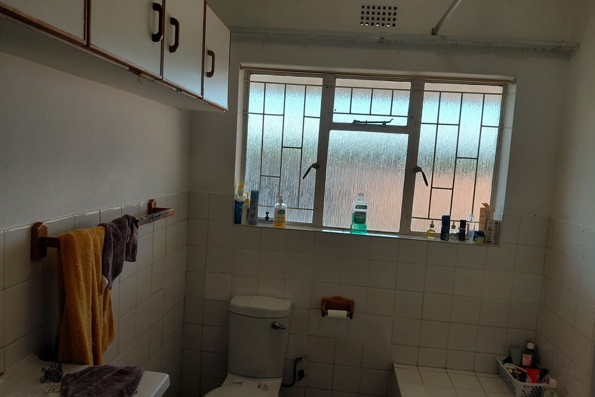 A dated bathroom featuring white wall tiles, a standard toilet, a bathtub, and overhead storage cabinetry with a window providing natural light.