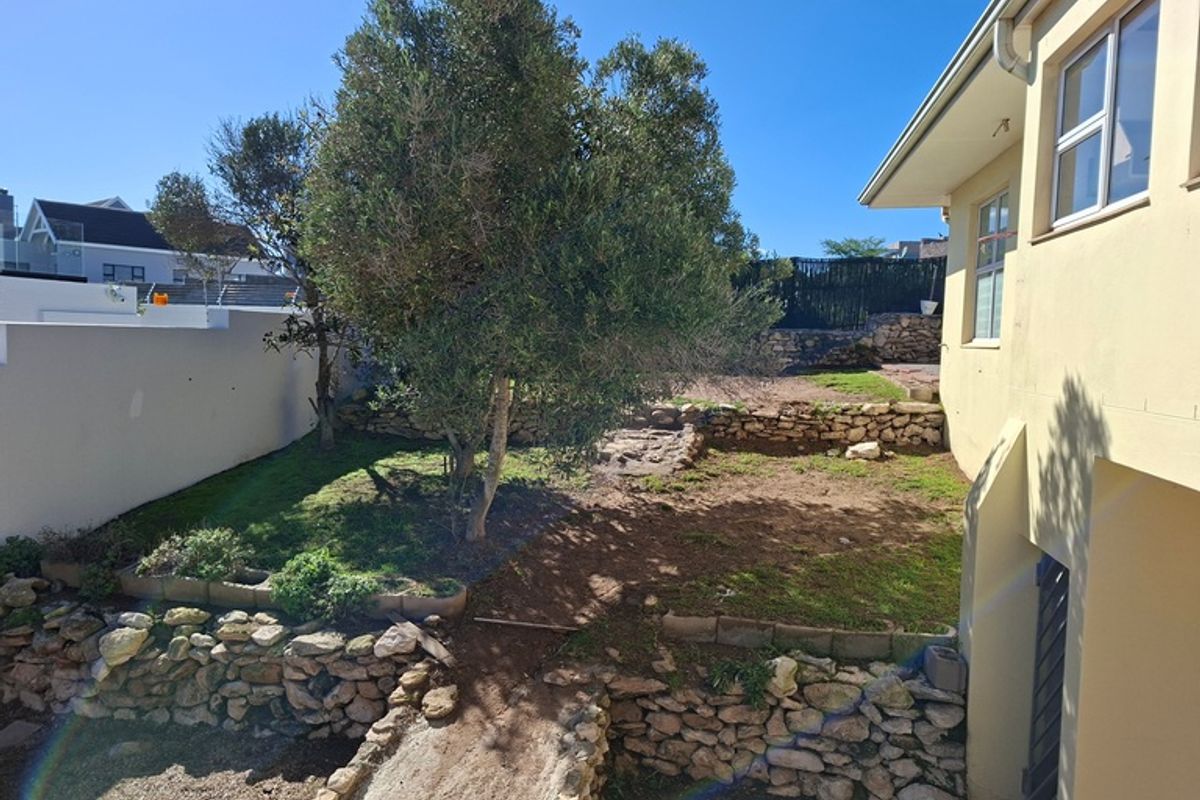 A rear garden area featuring tiered stone retaining walls, established trees, and a multi-level landscape design adjacent to the house exterior.