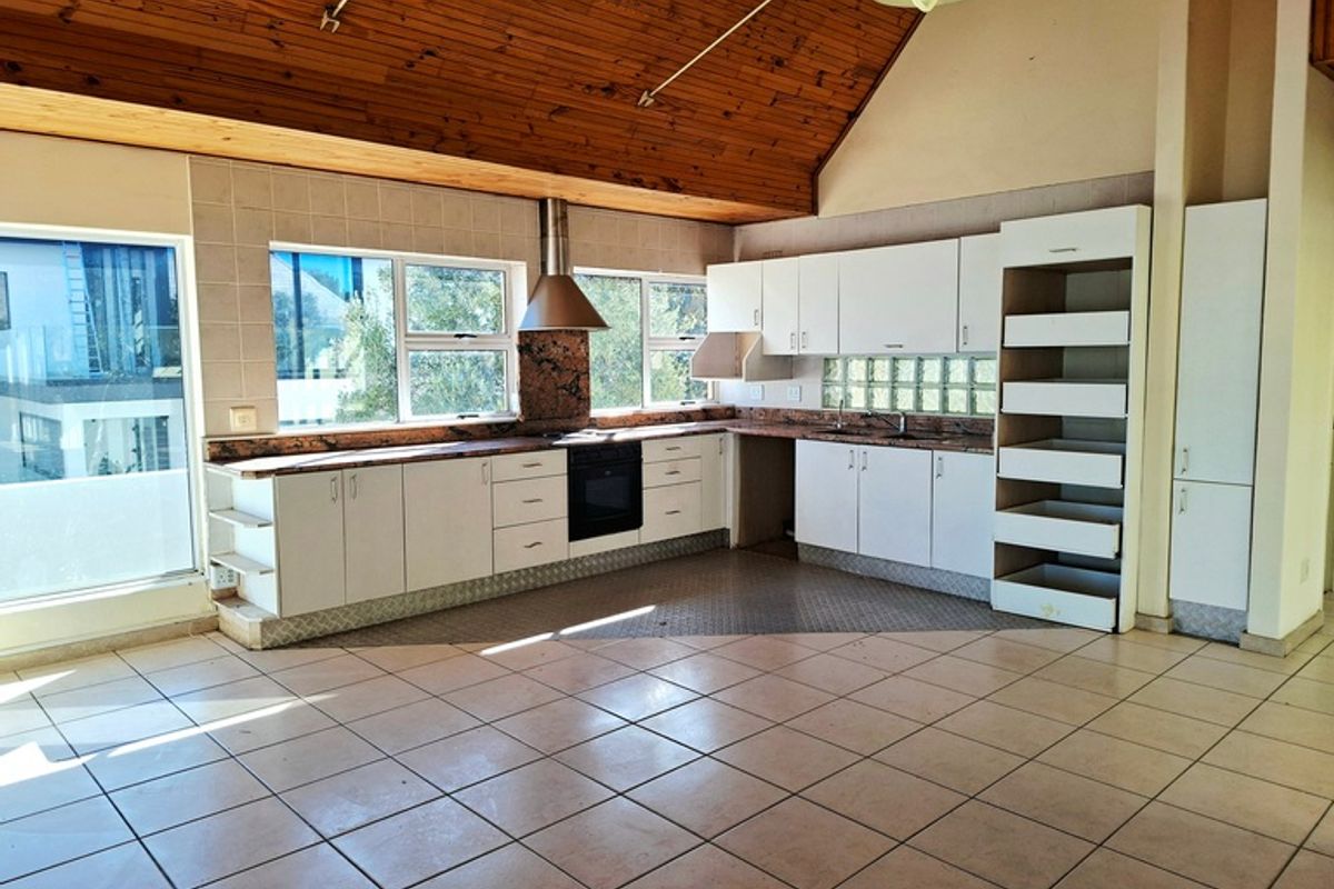 Spacious kitchen featuring a high vaulted timber ceiling, tiled flooring, built-in cabinetry, and a stainless steel extractor fan.