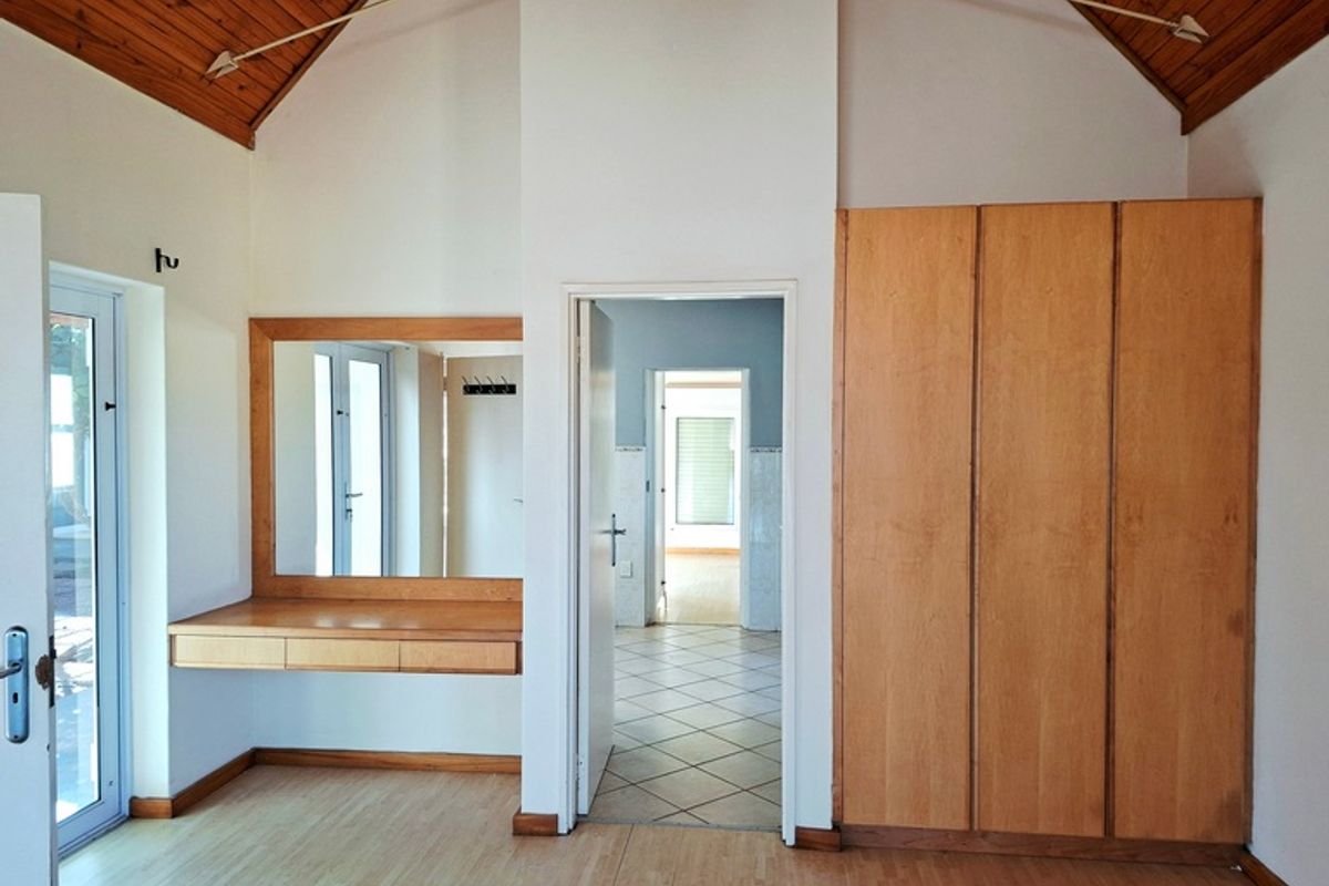 Bedroom featuring a vaulted timber ceiling, built-in wooden wardrobe, and a wall-mounted vanity unit with mirror, providing access to an adjoining tiled room.