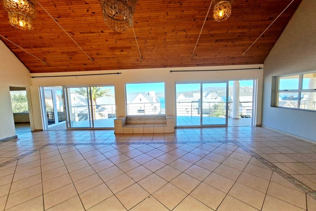 Spacious living area featuring high vaulted timber ceilings, tiled flooring, and large sliding glass doors opening onto a balcony with coastal views.
