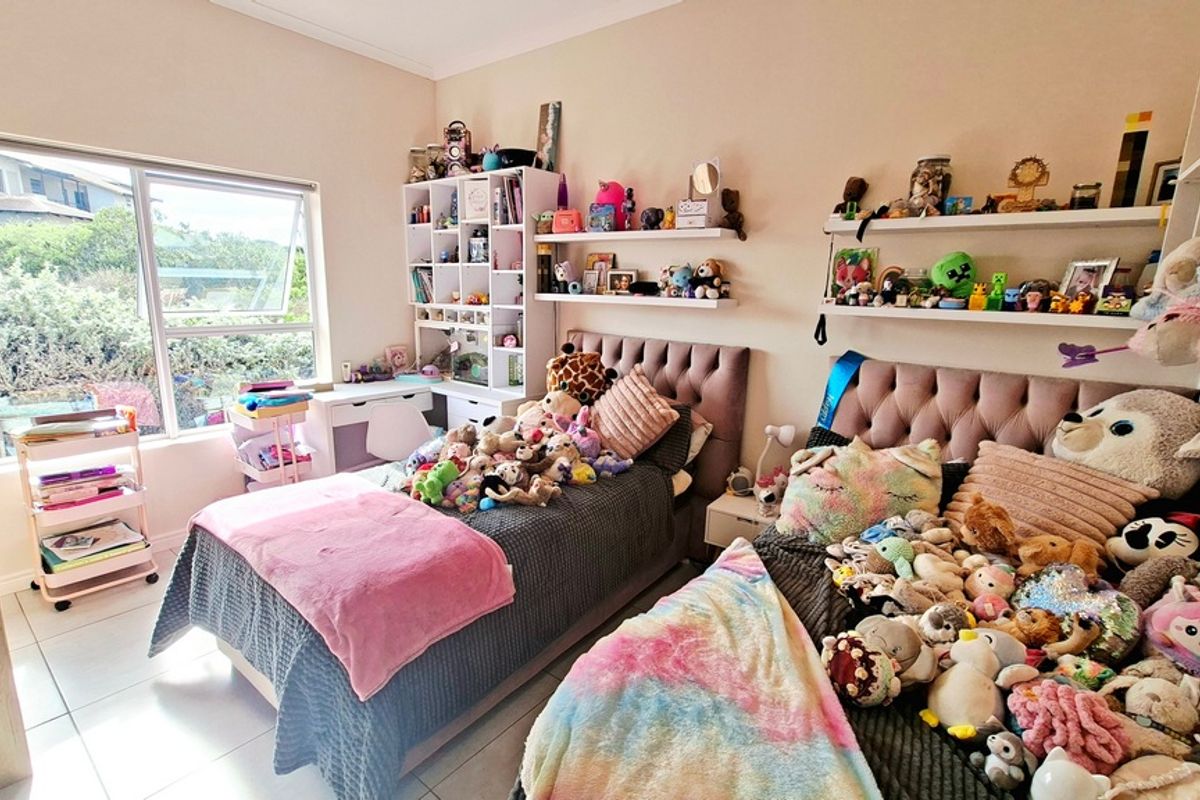 A bright bedroom featuring tiled flooring, built-in shelving units, and large windows providing natural light and garden views.