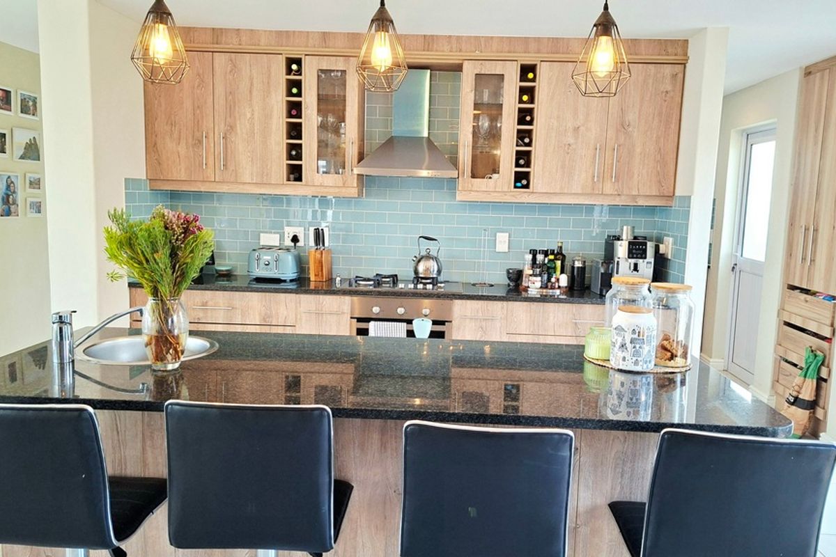 Modern kitchen featuring light wood cabinetry, a dark granite island with integrated sink, subway tile backsplash, and stainless steel extractor fan.