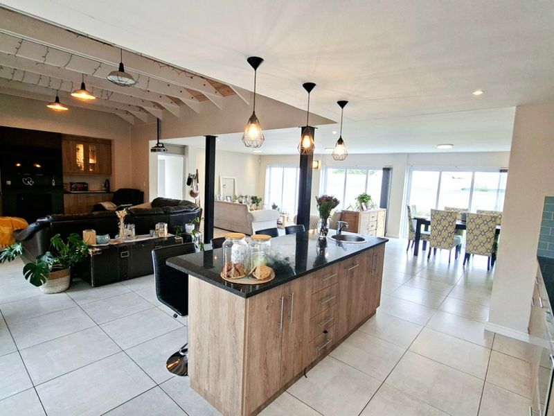 Spacious open-plan living area featuring a modern kitchen with a central island, granite countertops, and tiled flooring throughout, flowing into the dining and lounge spaces.
