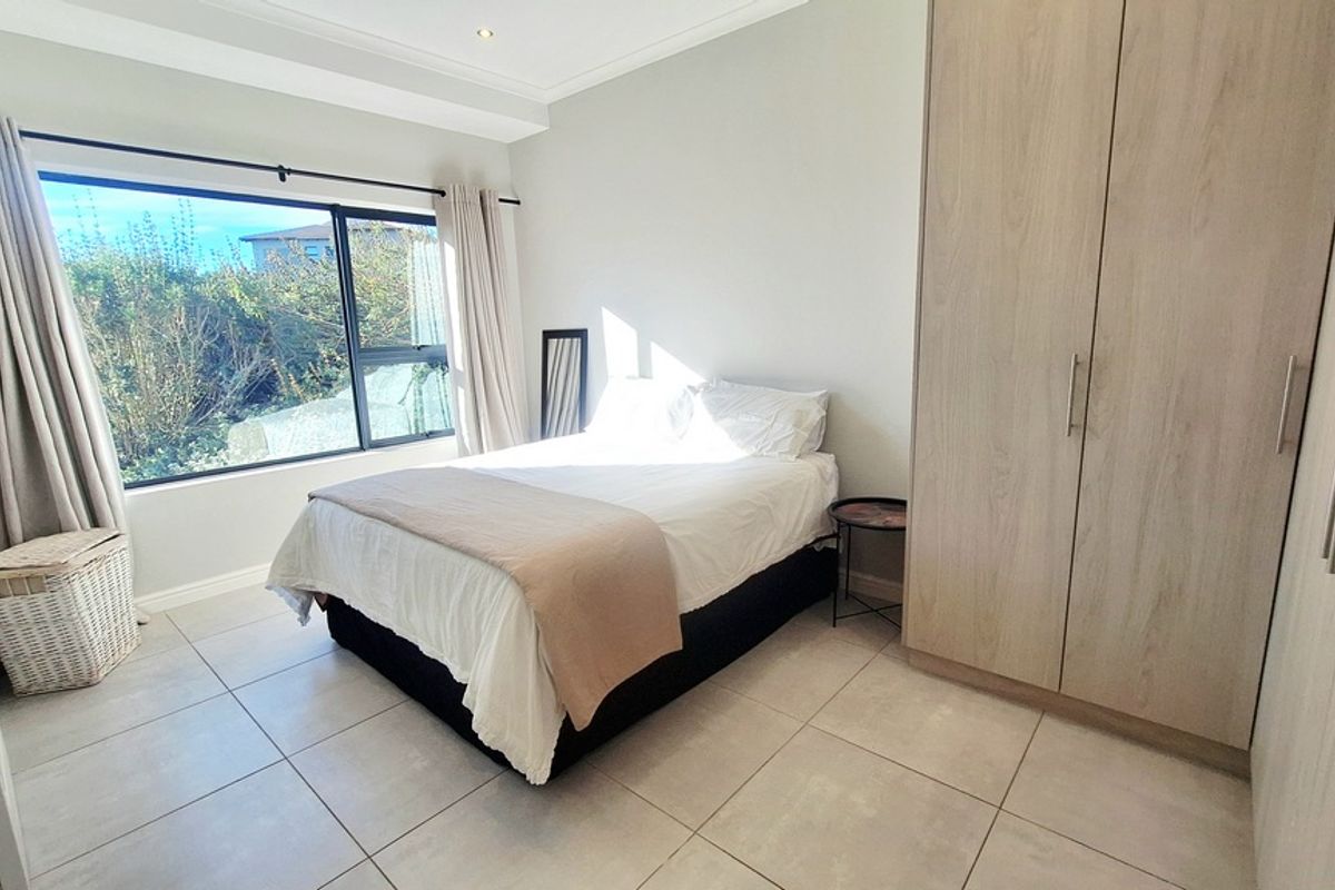 A bright and modern bedroom featuring neutral floor tiles, built-in wooden cabinetry, and large windows allowing for ample natural light.