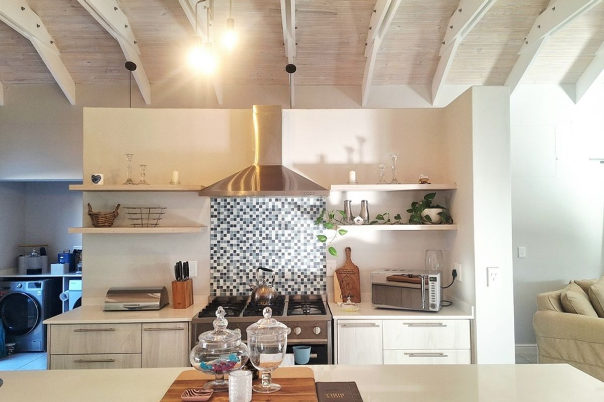 Modern open-plan kitchen featuring a stainless steel extractor fan, mosaic tile backsplash, floating timber shelving, and a vaulted timber-beamed ceiling.