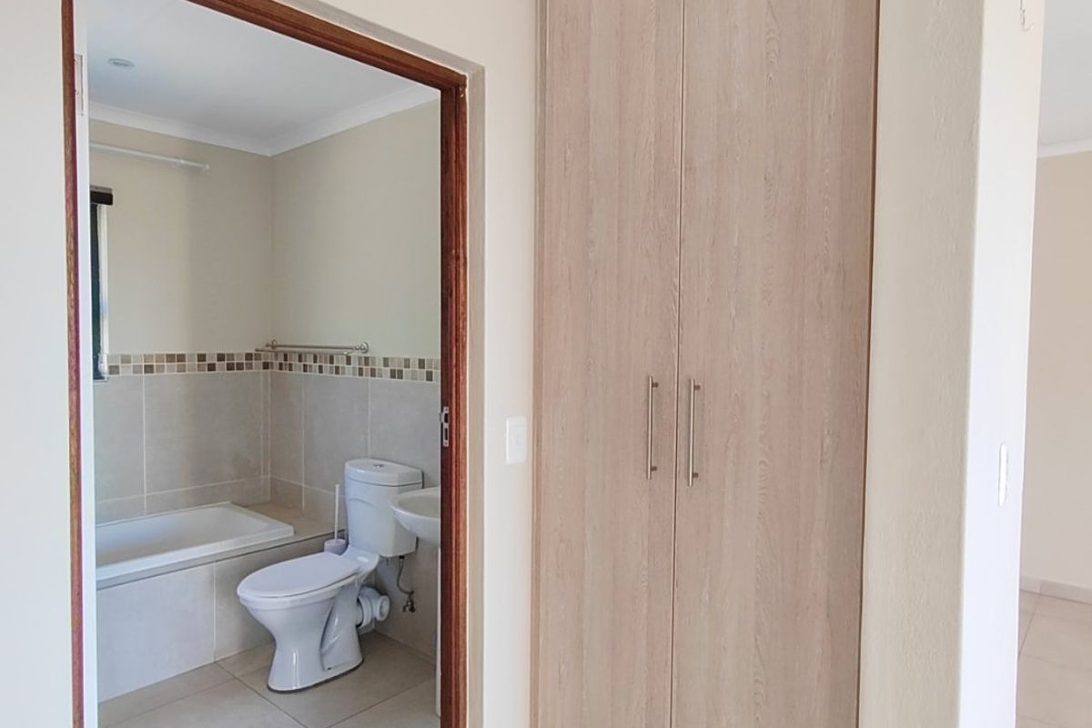 A view of a bathroom featuring a built-in bathtub and toilet, adjacent to a hallway with built-in wooden cabinetry.