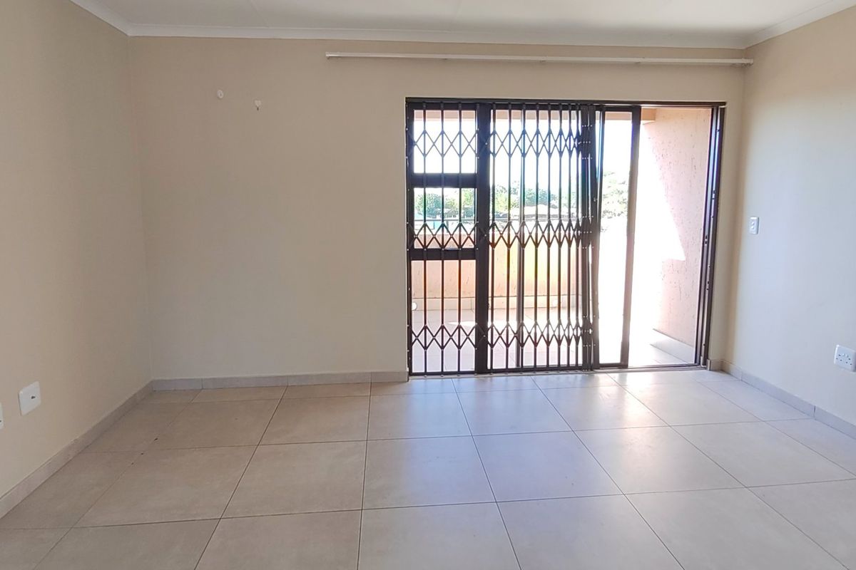 A bright, empty living area featuring neutral floor tiles and a sliding door with a security gate leading to an outdoor space.