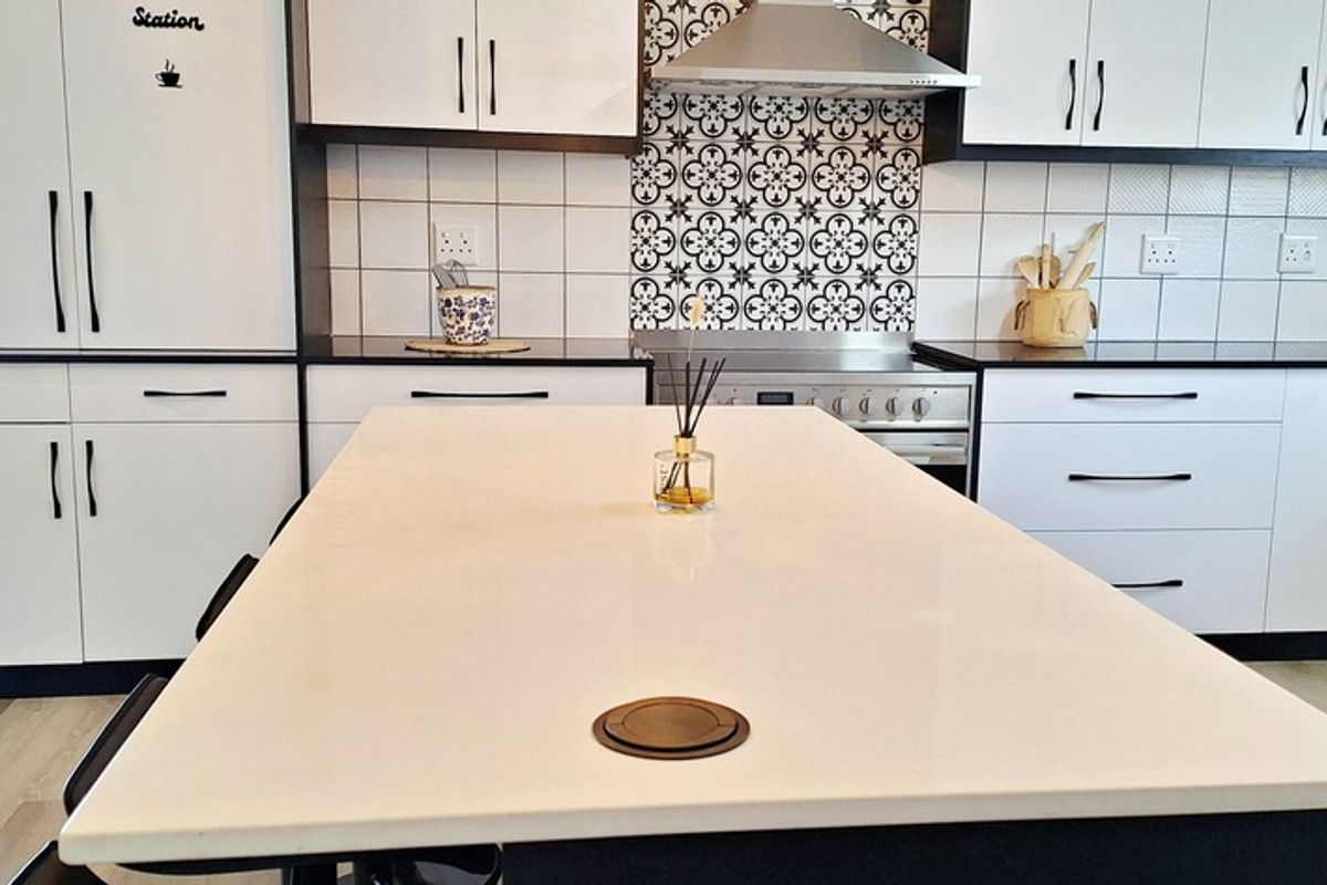 Modern kitchen featuring a central island with stone countertop, white cabinetry, stainless steel extractor fan, and decorative tiled backsplash.