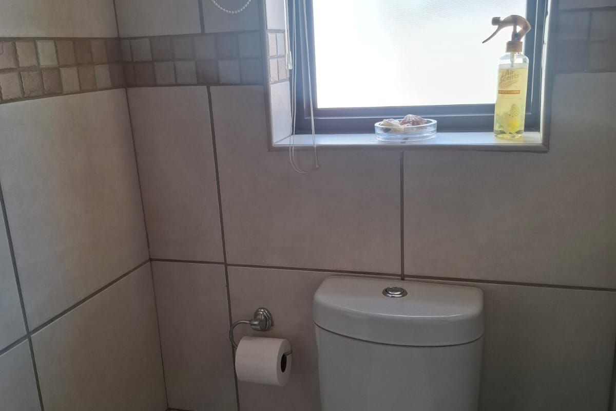 A functional bathroom featuring floor-to-ceiling wall tiles, a modern toilet, and a window providing natural light.