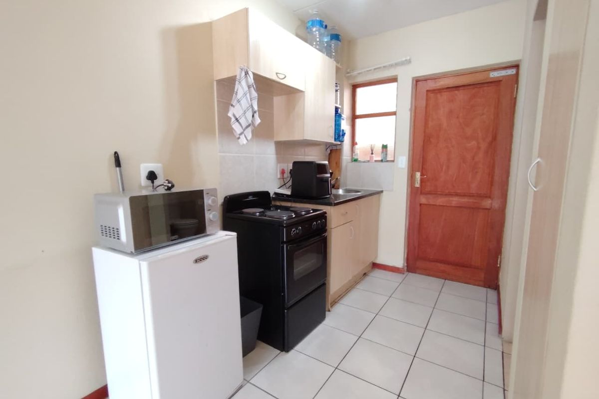 Compact kitchen featuring light wood cabinetry, tiled flooring, a freestanding stove, and a wooden door leading to the exterior.
