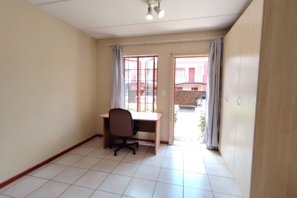 A functional bedroom featuring tiled flooring, built-in cupboards, and direct access to an outdoor area through a glass door.