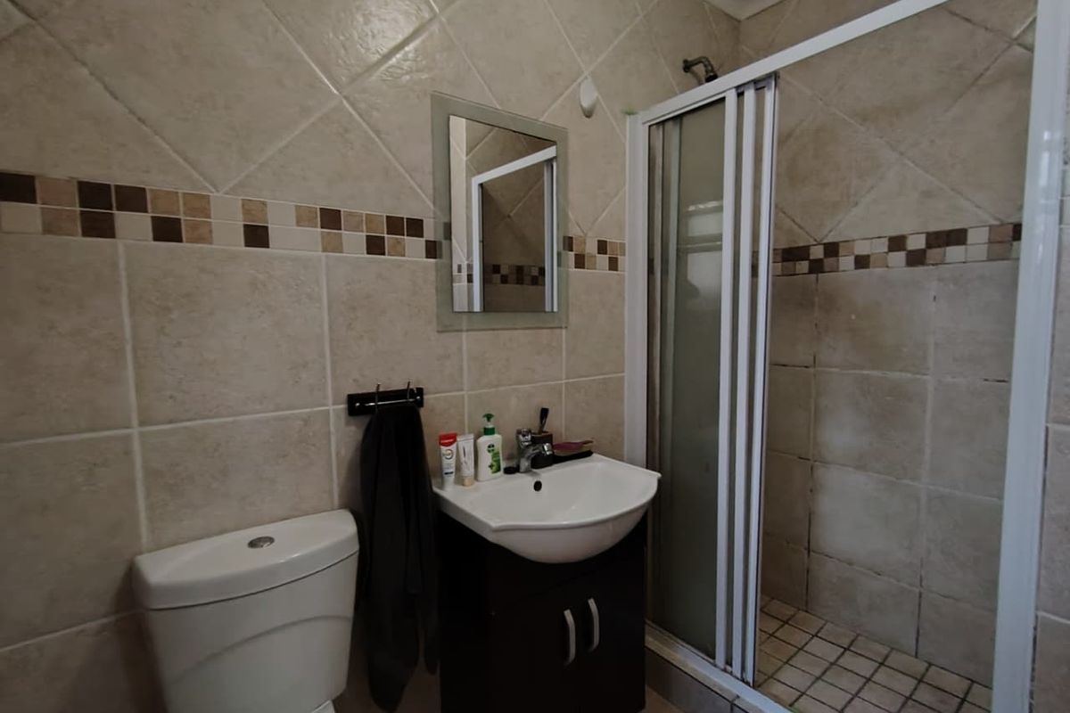 A compact bathroom featuring a tiled shower enclosure, a vanity basin with storage, and a standard toilet, finished with neutral wall tiles.