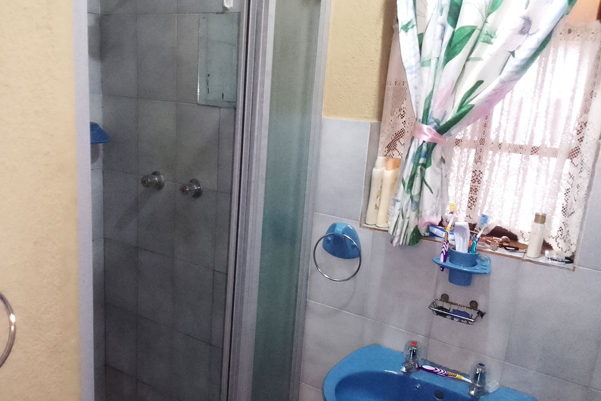 A compact bathroom featuring a shower enclosure with tiled walls and a blue pedestal basin, requiring cosmetic updates to modernize the space.