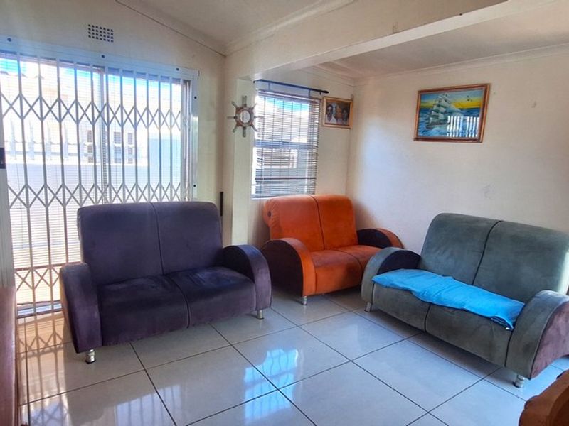 A living room featuring tiled flooring, a security gate, and natural light through windows and a timber door.