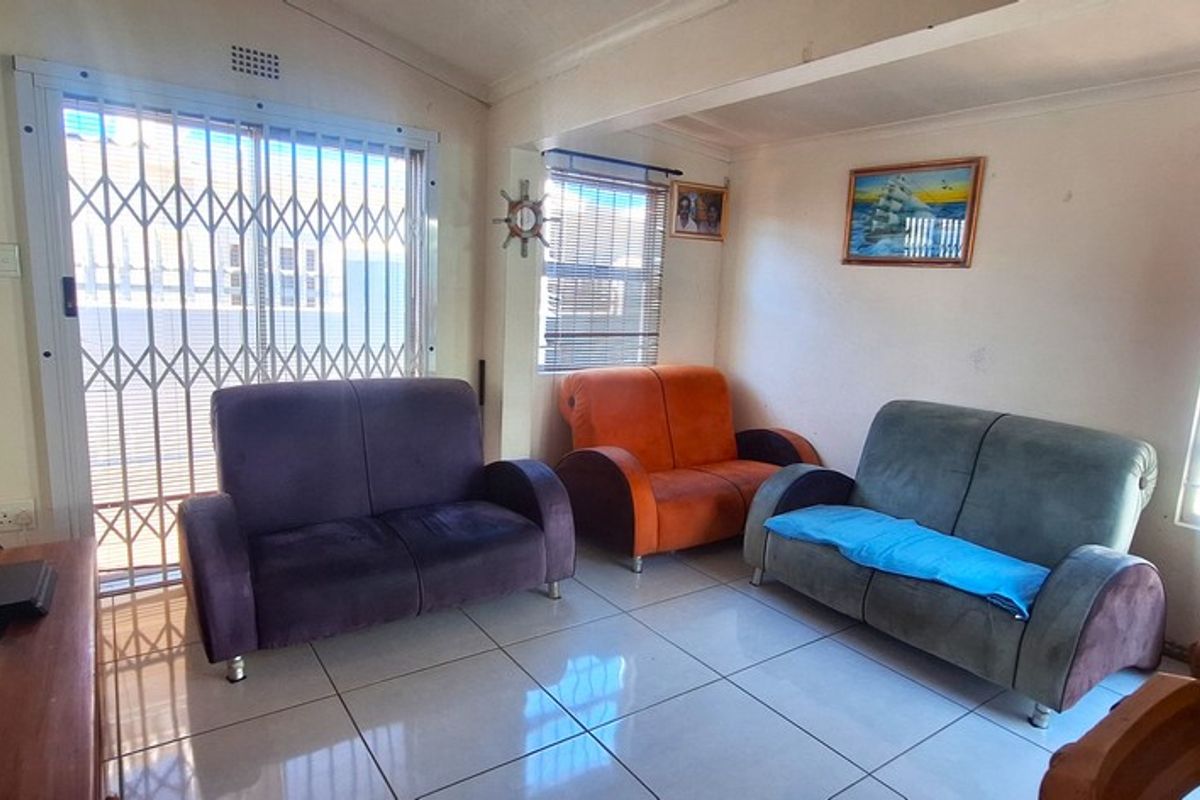 A living room featuring tiled flooring, a security gate, and natural light through windows and a timber door.