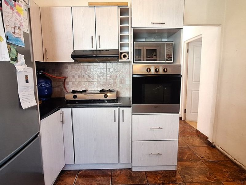 Compact kitchen featuring light-toned cabinetry, a built-in oven, gas hob, extractor fan, and tiled flooring with a neutral backsplash.