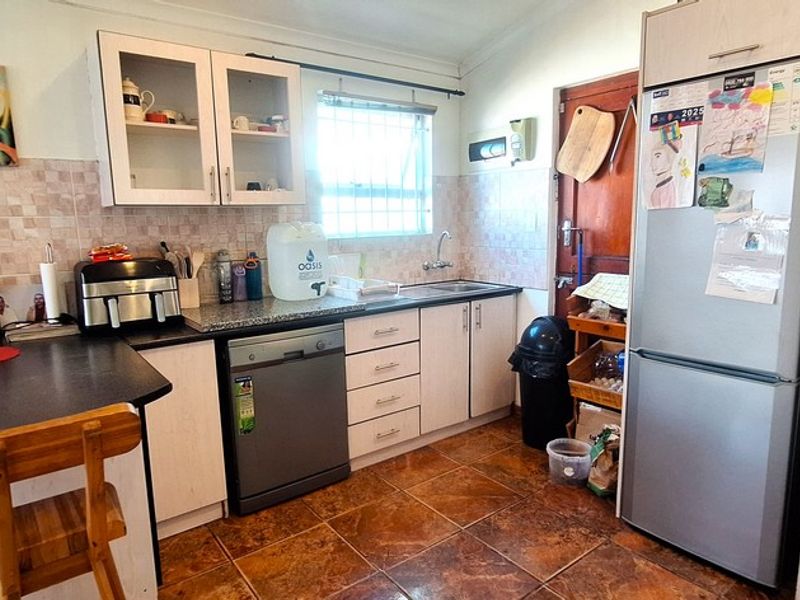 A functional kitchen featuring built-in cabinetry, tiled backsplash, and tiled flooring, offering a practical layout with integrated appliance space.