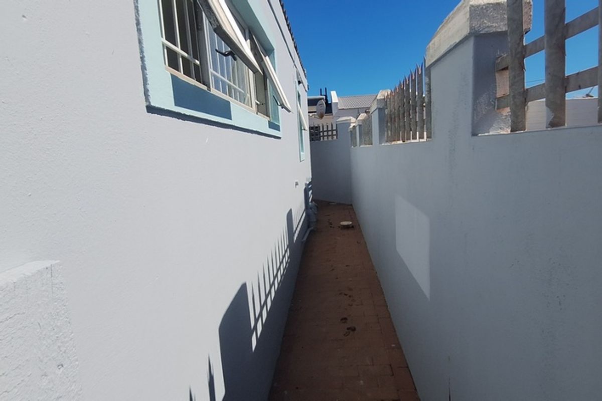 A narrow side passage featuring paved flooring, boundary walls with security spikes, and trellis fencing.