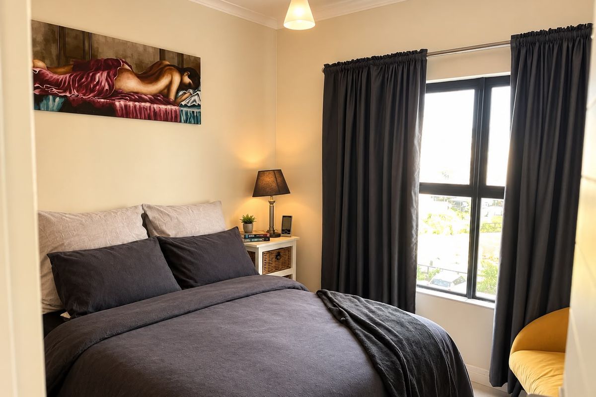 A cozy bedroom featuring neutral walls, a window with dark curtains, and a central ceiling light fixture.