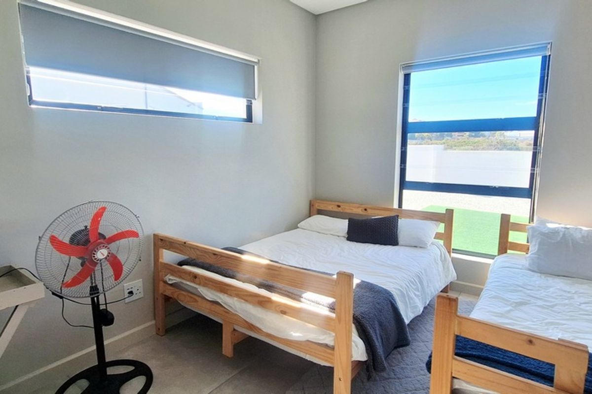 A bright and modern bedroom featuring large windows with roller blinds, neutral wall finishes, and tiled flooring.