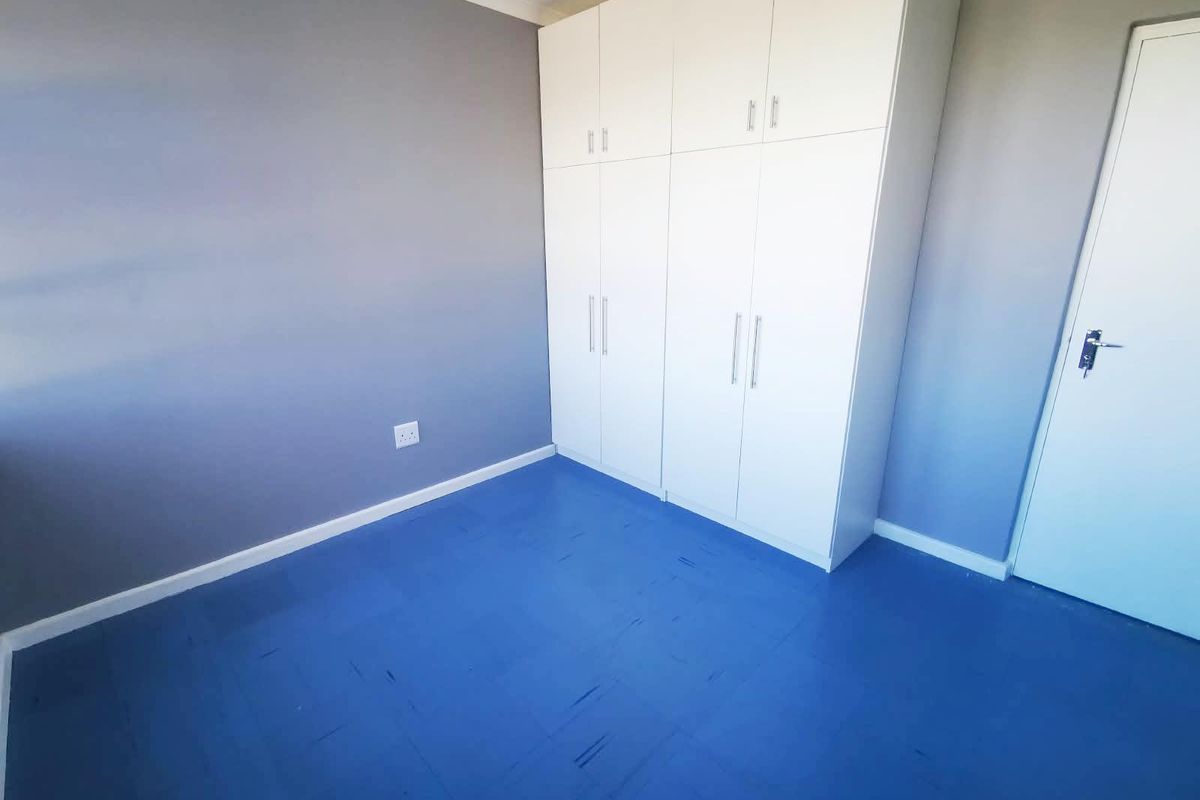 A clean, empty bedroom featuring built-in white cupboards and blue vinyl flooring, offering a neutral space ready for personalization.