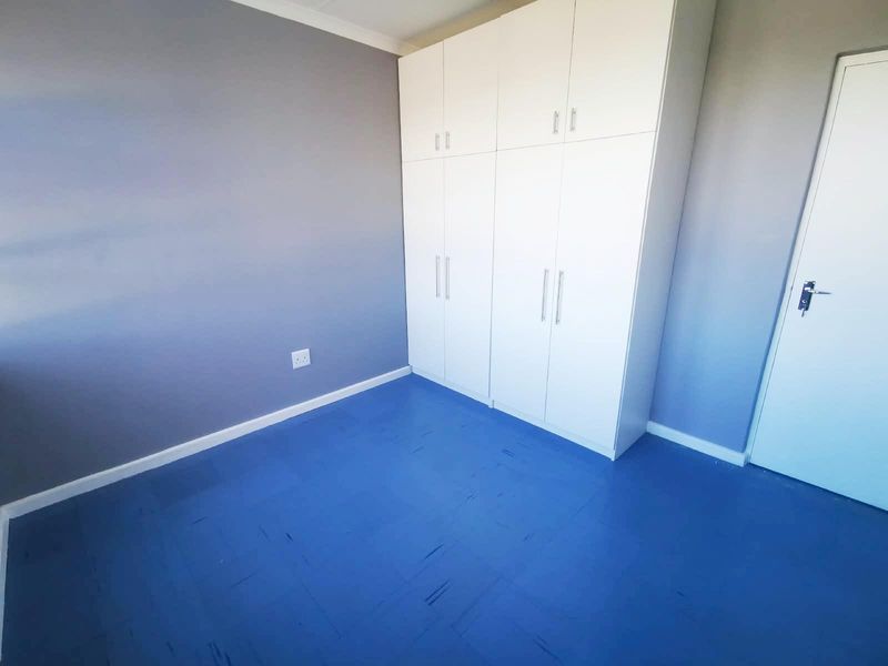A clean, empty bedroom featuring built-in white cupboards and blue vinyl flooring, offering a neutral space ready for personalization.