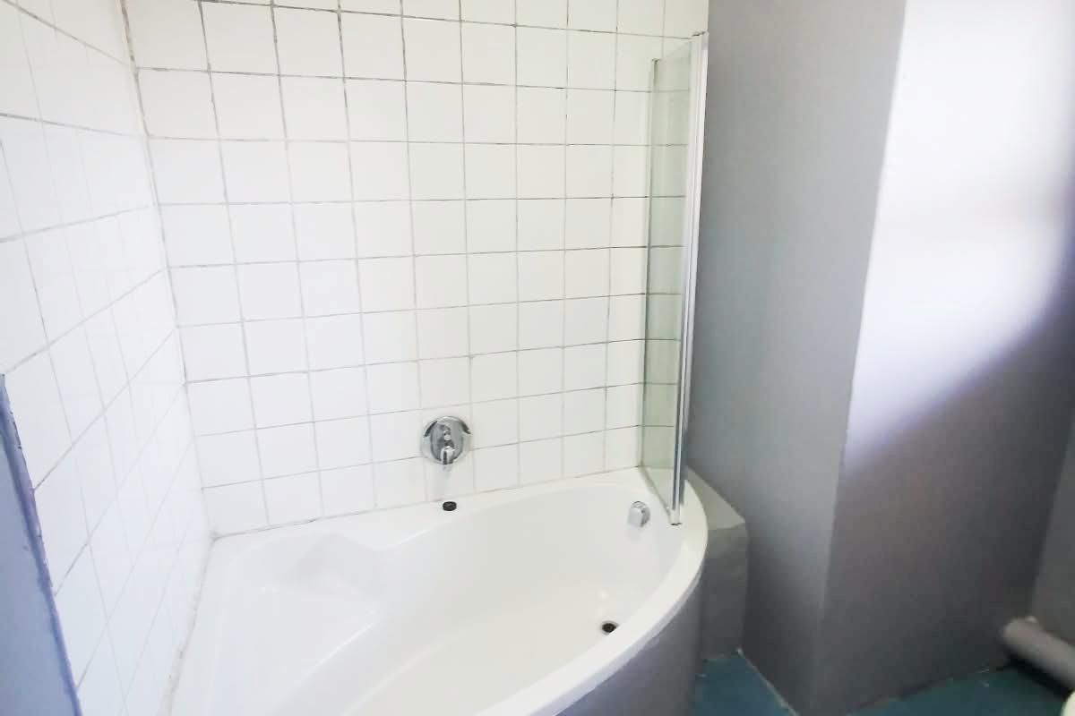 Bathroom featuring a corner bathtub with a shower head, glass screen, and tiled splashback, requiring cosmetic updates to the flooring and grout.