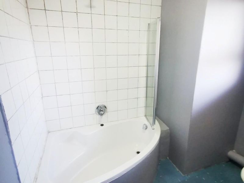 Bathroom featuring a corner bathtub with a shower head, glass screen, and tiled splashback, requiring cosmetic updates to the flooring and grout.
