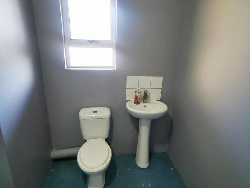 A compact bathroom featuring a pedestal basin with a tiled splashback and a standard toilet, finished with grey walls and blue floor tiles.